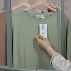 Close-up of a hand checking a price tag on a t-shirt in a minimalist clothing store.